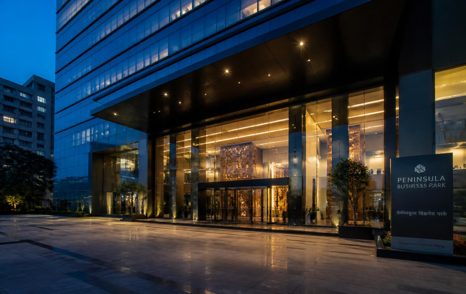 Illuminated glass corporate office tower entrance at blue hour